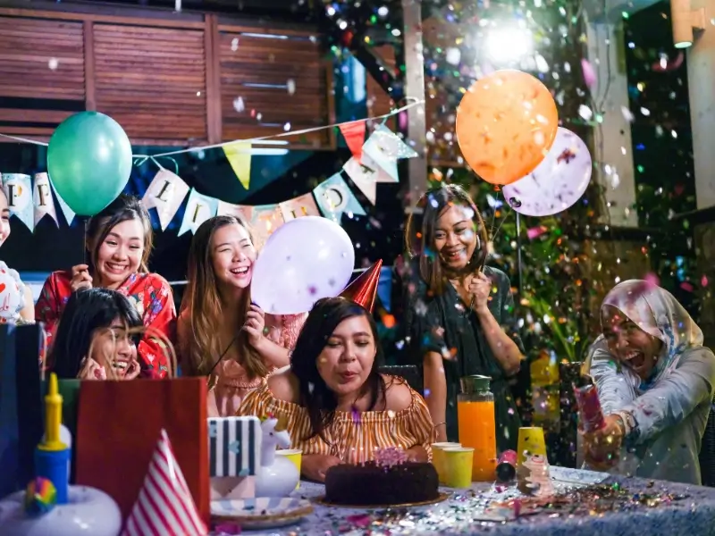 Friends celebrating a birthday while a woman blows out candles on a cake for A2 writing example 'My favourite photograph'