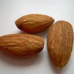 Close-up photo of three raw almonds on a white background.